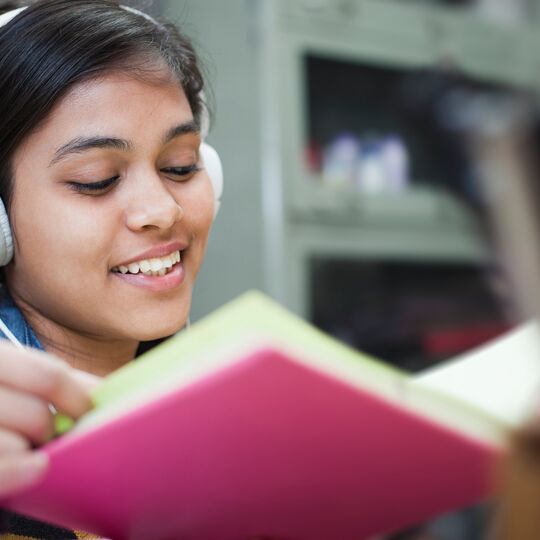 Lächelndes Mädchen mit Kopfhörern und aufgeschlagenem Buch